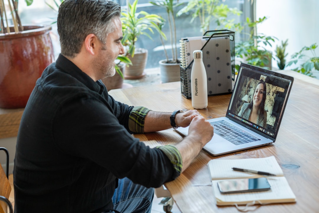 Video meeting; man in dark shirt sitting at table in front of a laptop with a female on the screen